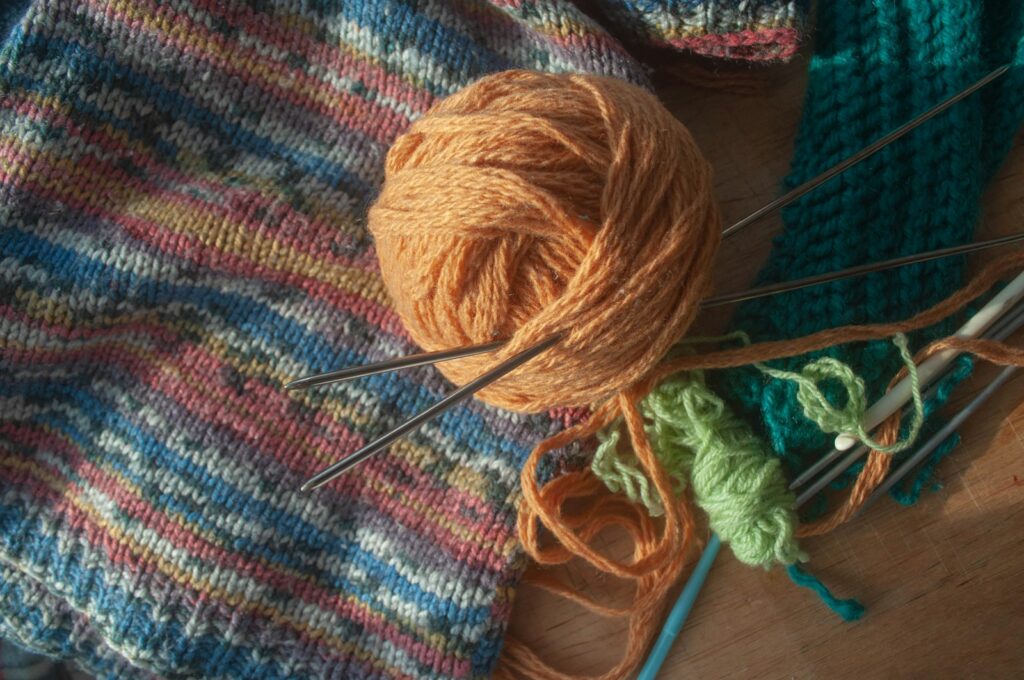 Ball of yarn and knitting needles resting on a table alongside other crafting tools