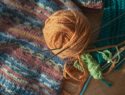 Ball of yarn and knitting needles resting on a table alongside other crafting tools