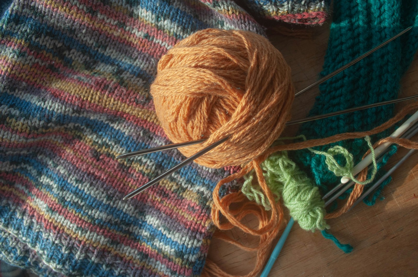 Ball of yarn and knitting needles resting on a table alongside other crafting tools