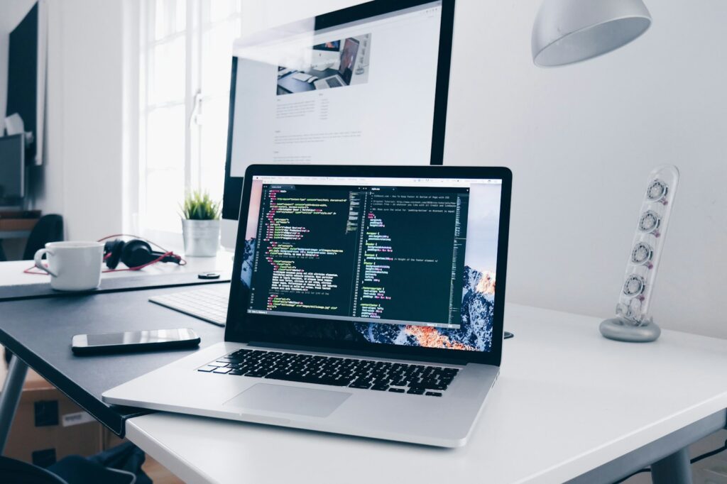 MacBook displaying lines of code on a busy desk, representing website maintenance