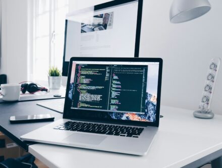 MacBook displaying lines of code on a busy desk, representing website maintenance