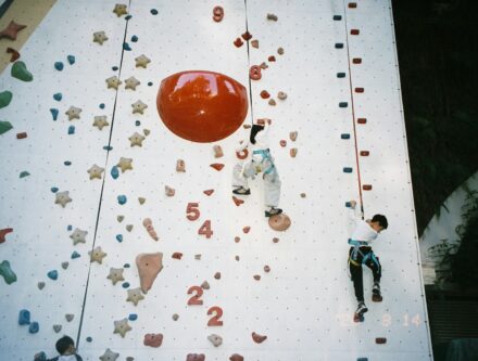 Children climbing a colourful indoor rock wall, as at a climbing wall party