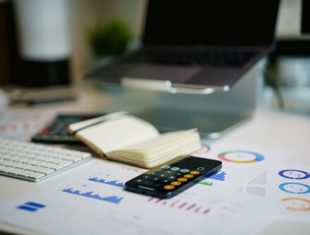 Office desk with a smartphone and financial charts, representing a firm's compliance paperwork