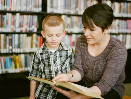 Woman and young child reading a book together in a library
