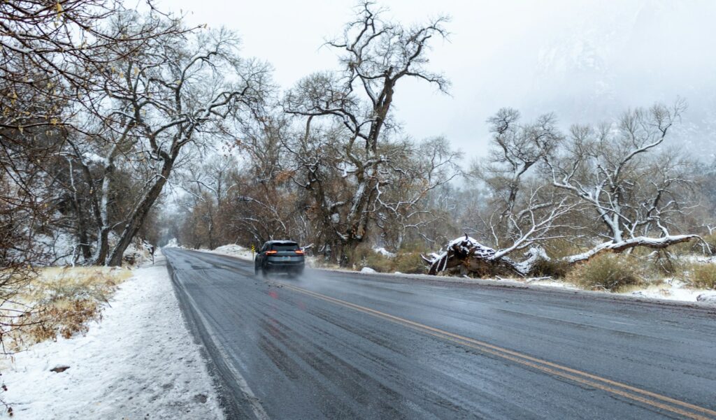 Car driving along a wet road with patches of snow piled either side in winter