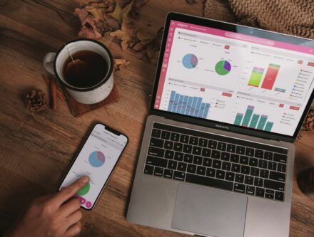 Laptop and smartphone showing business analytics dashboards on a wooden desk with a mug