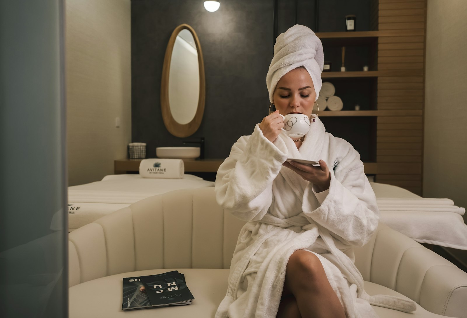 Woman in a white robe sitting on a white couch, relaxing during a spa break