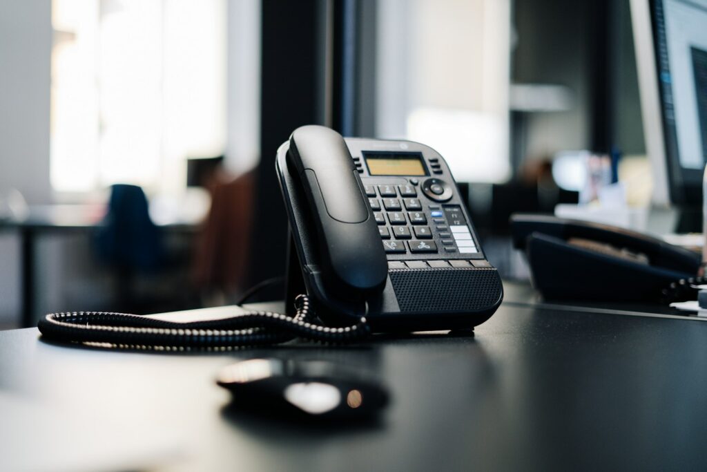 Black desk phone on a dark wooden table, the sort of line an AI receptionist answers