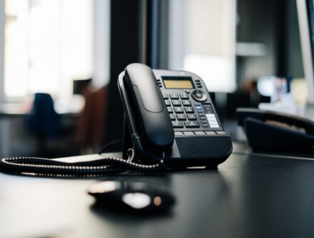 Black desk phone on a dark wooden table, the sort of line an AI receptionist answers