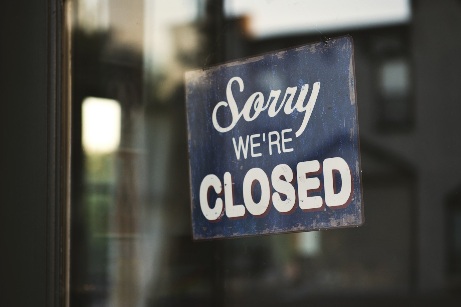 Sorry we're closed sign hanging on a glass shop door
