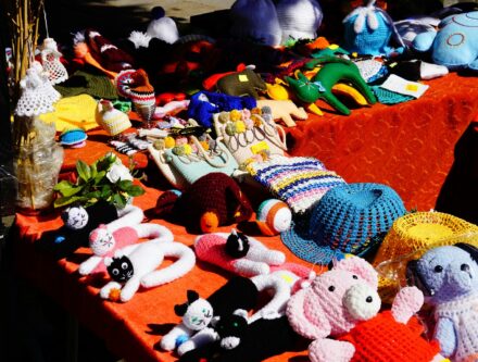 Handmade crochet toys and hats displayed on an orange tablecloth at an outdoor market