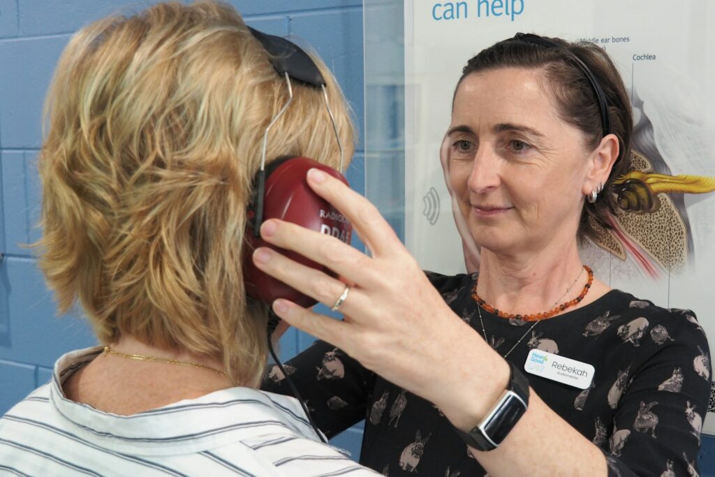 Audiologist placing headphones on a woman ready for her hearing test
