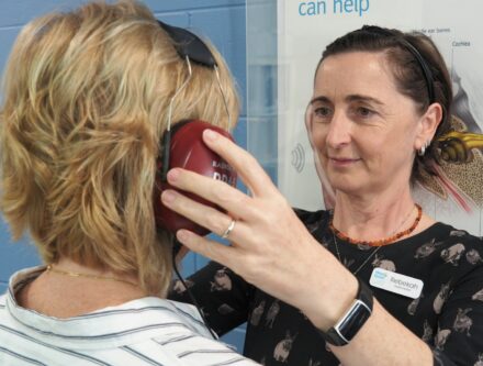 Audiologist placing headphones on a woman ready for her hearing test