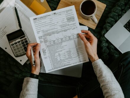 Hands holding tax forms beside a calculator and laptop, ready for an audit