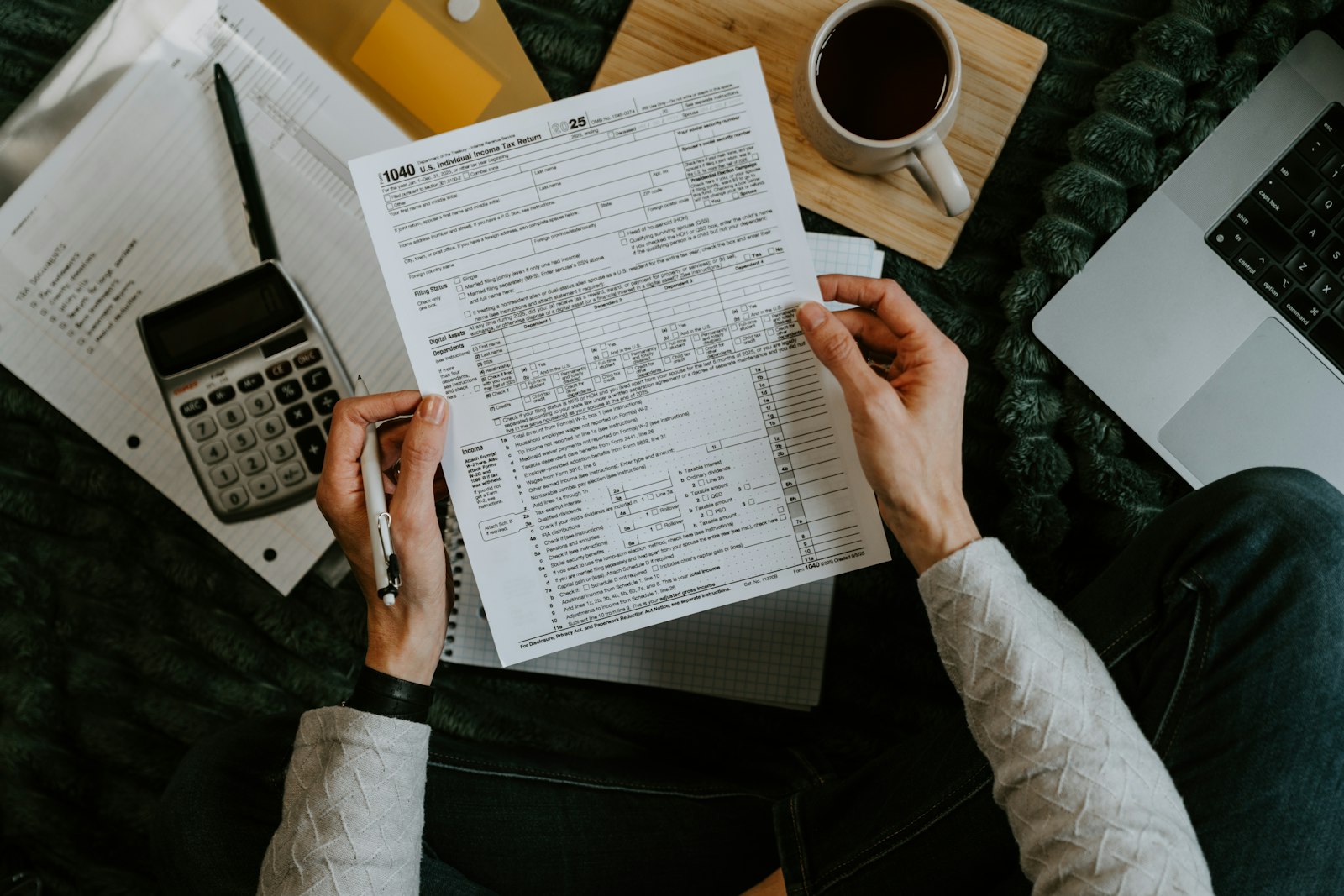 Hands holding tax forms beside a calculator and laptop, ready for an audit