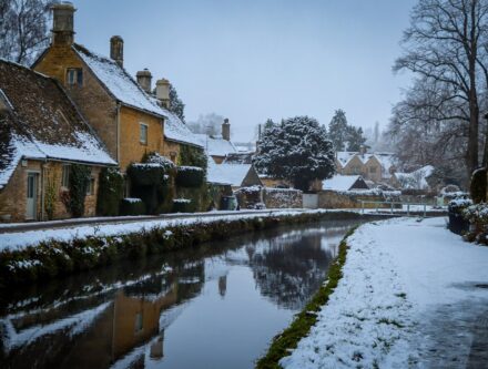 Stone cottages with snow-covered roofs beside a calm canal at Lower Slaughter in the Cotswolds