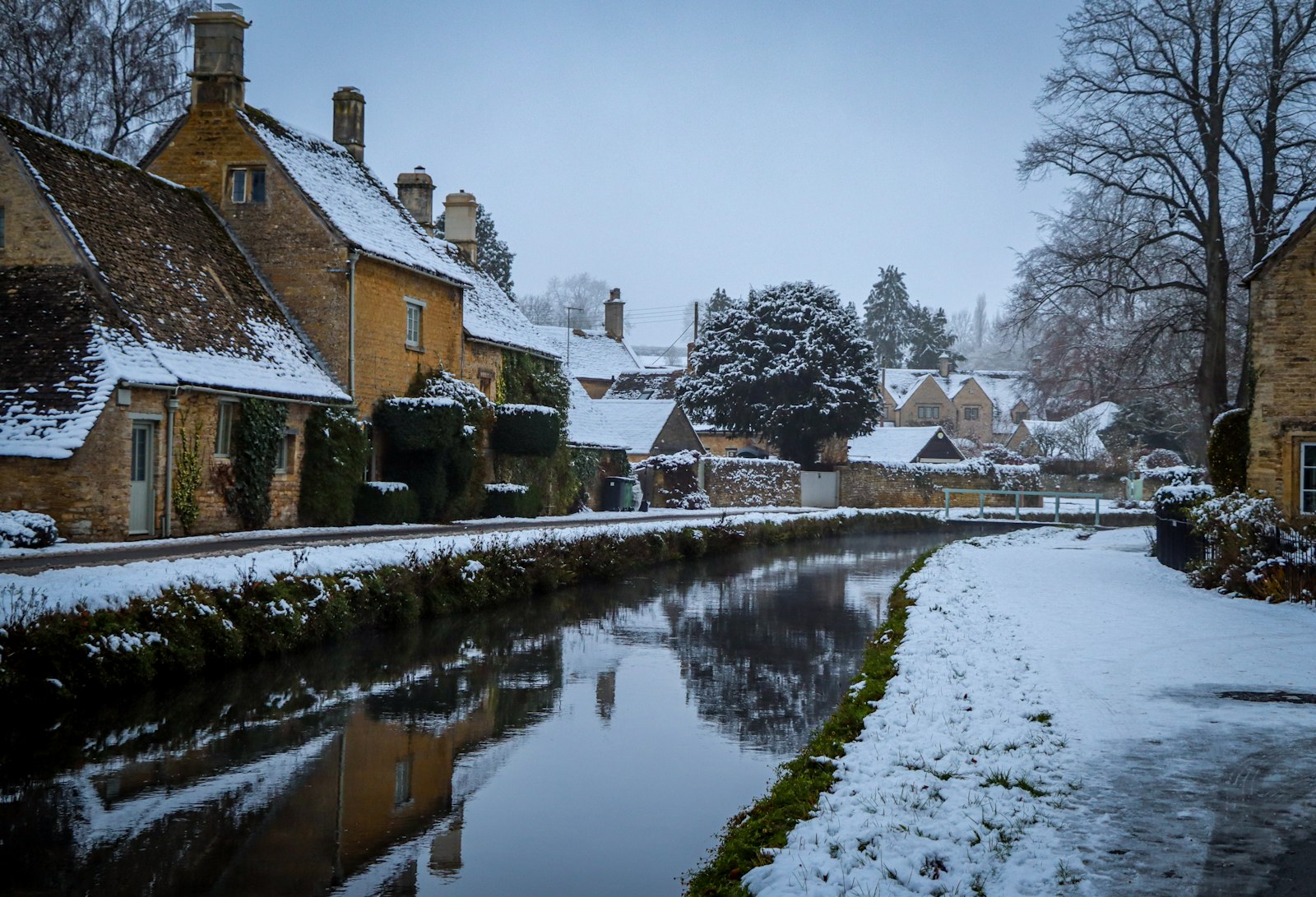 Stone cottages with snow-covered roofs beside a calm canal at Lower Slaughter in the Cotswolds